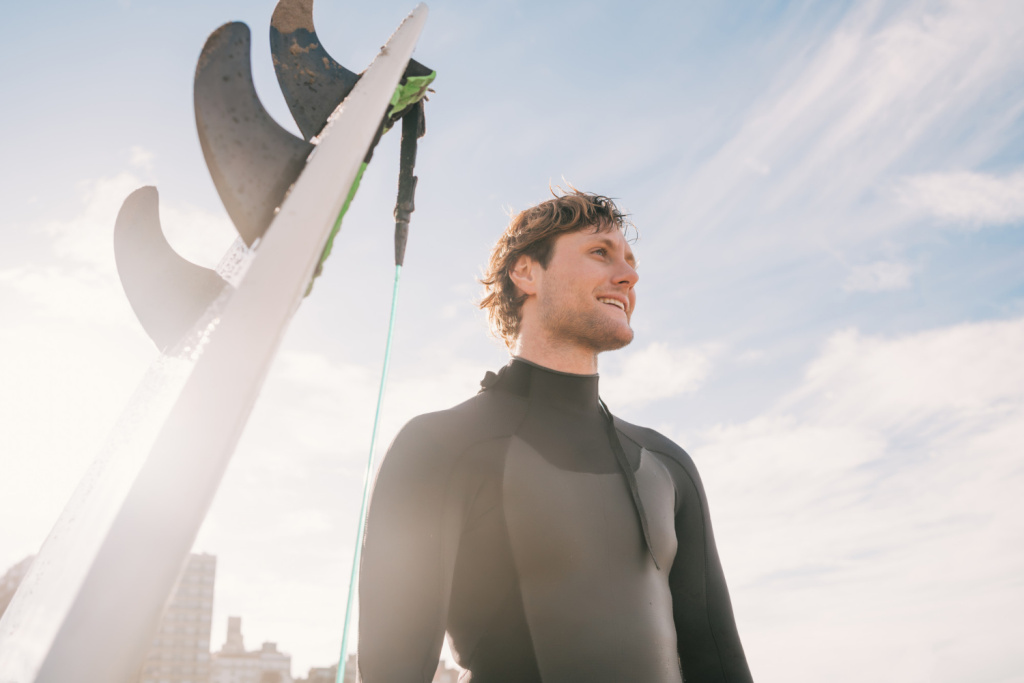close-up-of-young-surfer-standing-at-the-beach-next-to-his-surfboard-sport-and-water-sport-concept.jpg